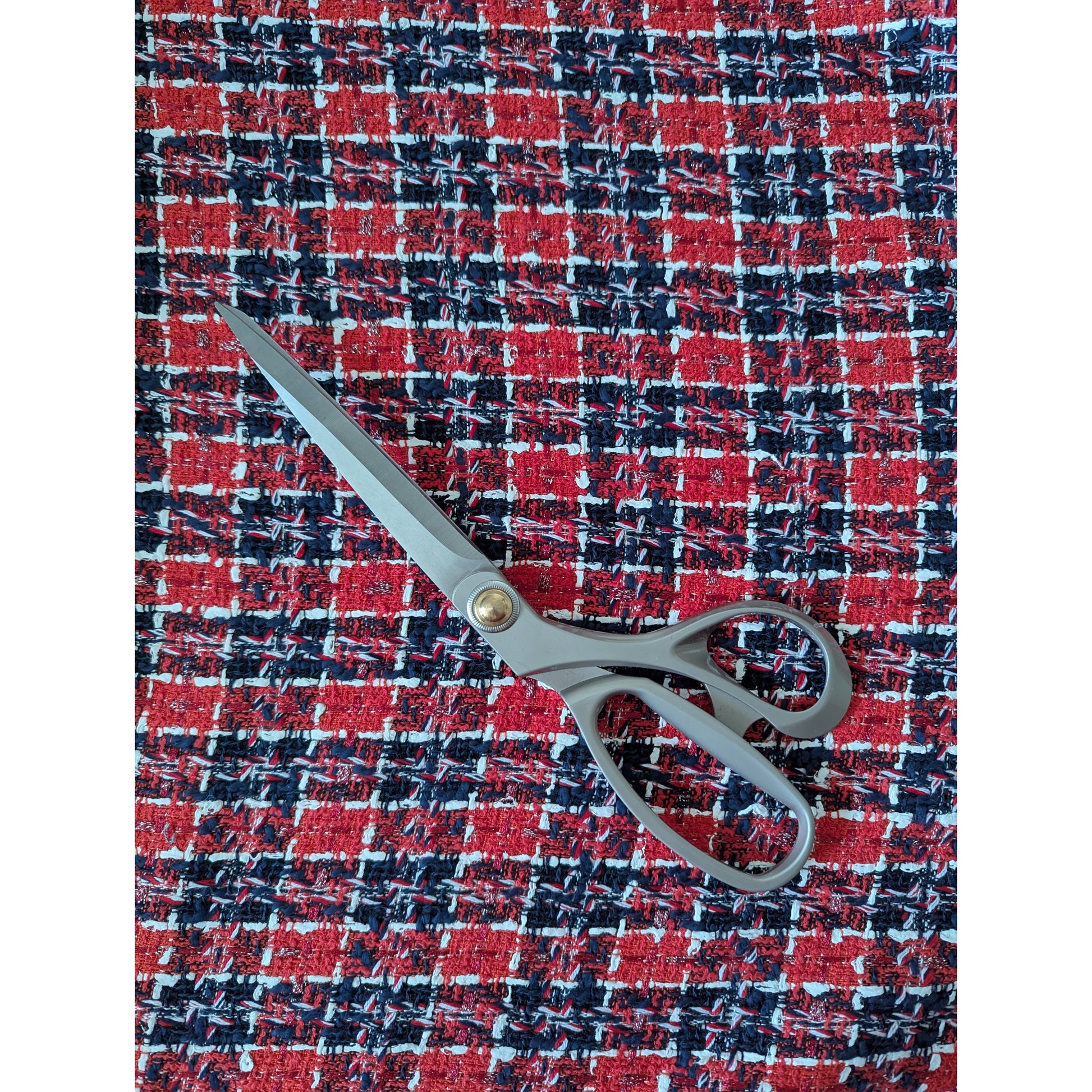 Red, black, and white plaid tweed fabric with a pair of grey sewing scissors.