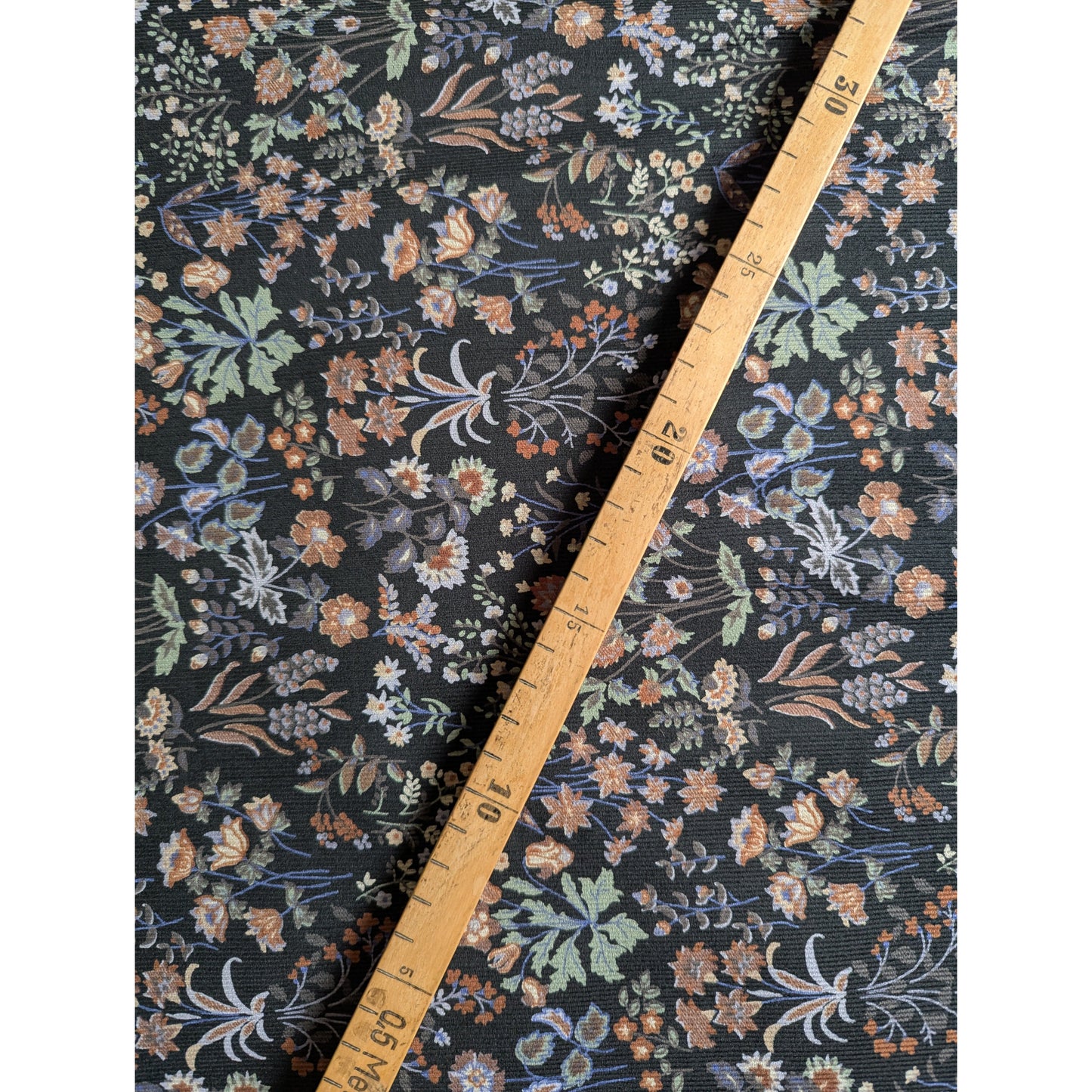 Black Feincord fabric with a vibrant multicolor millefleur floral pattern, measured by a wooden ruler.