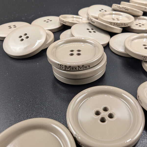 Beige Max Mara 3cm 4-hole buttons, smooth and round, with engraved logo, scattered on a dark surface.