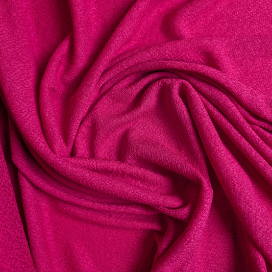 Fuchsia pink viscose crepe fabric, draped with soft folds, showing its textured surface.