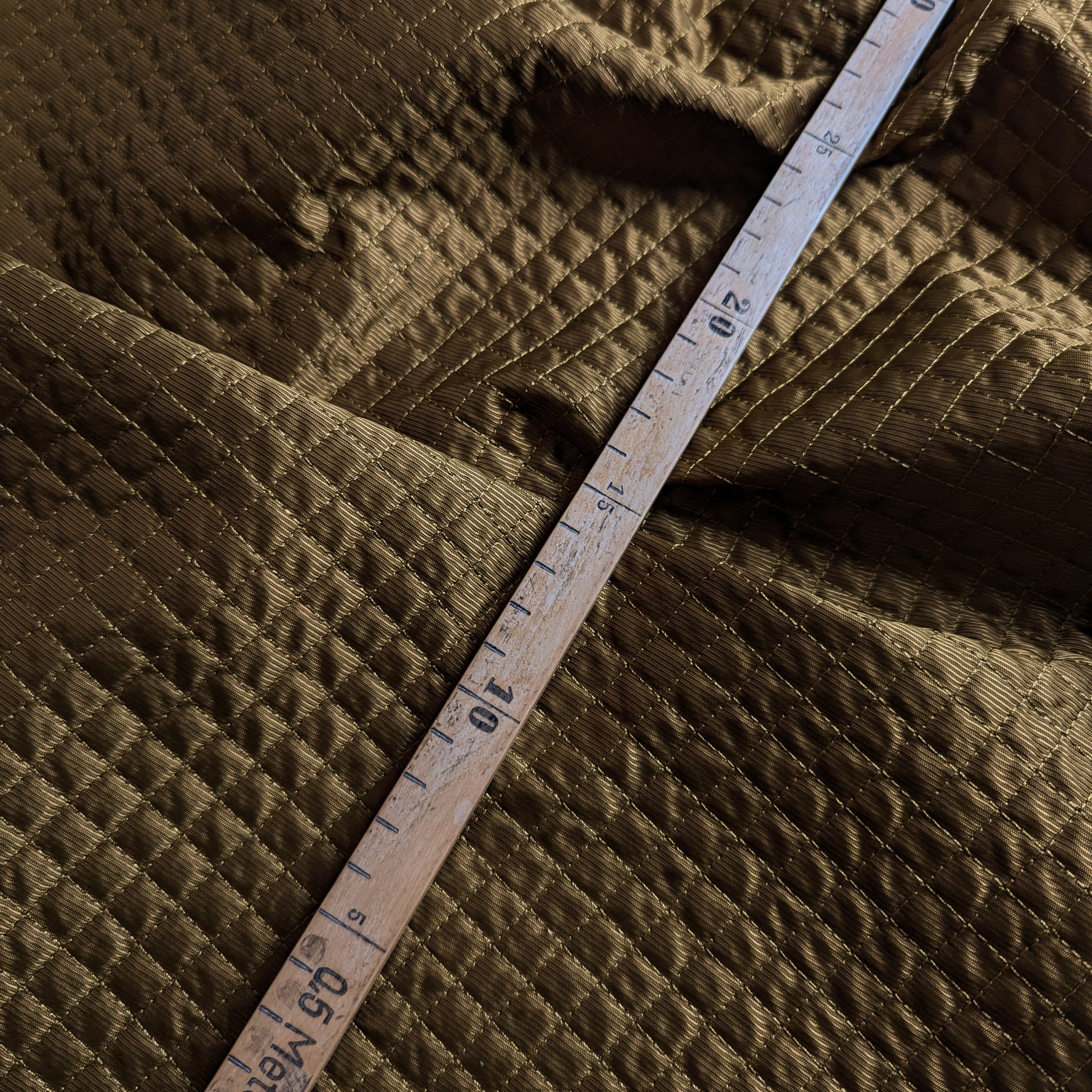 Luxurious olive green deadstock quilted fabric, matte textured and lightly padded, with a measuring tape.