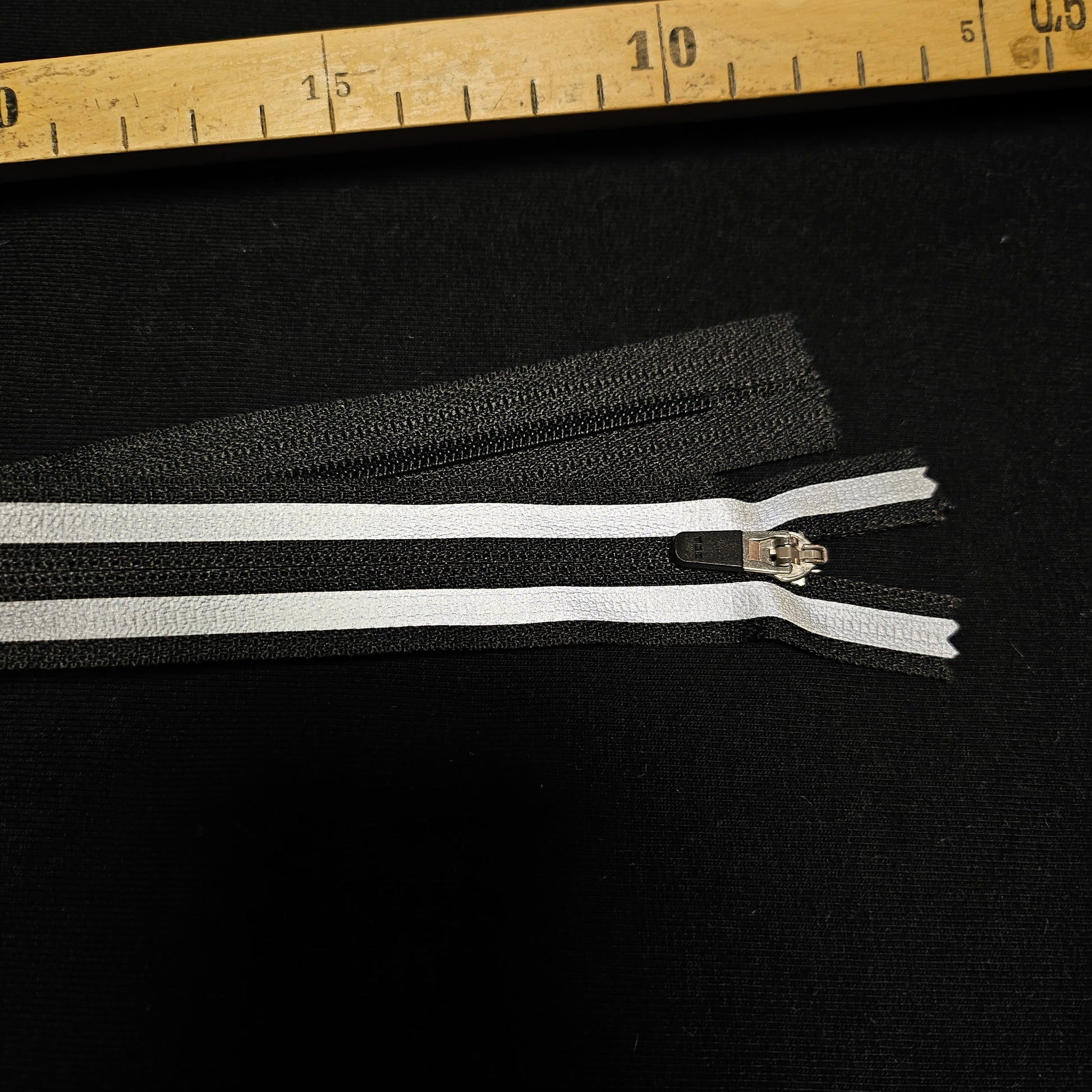 Black zipper with two white stripes and a silver pull, 30 cm long.