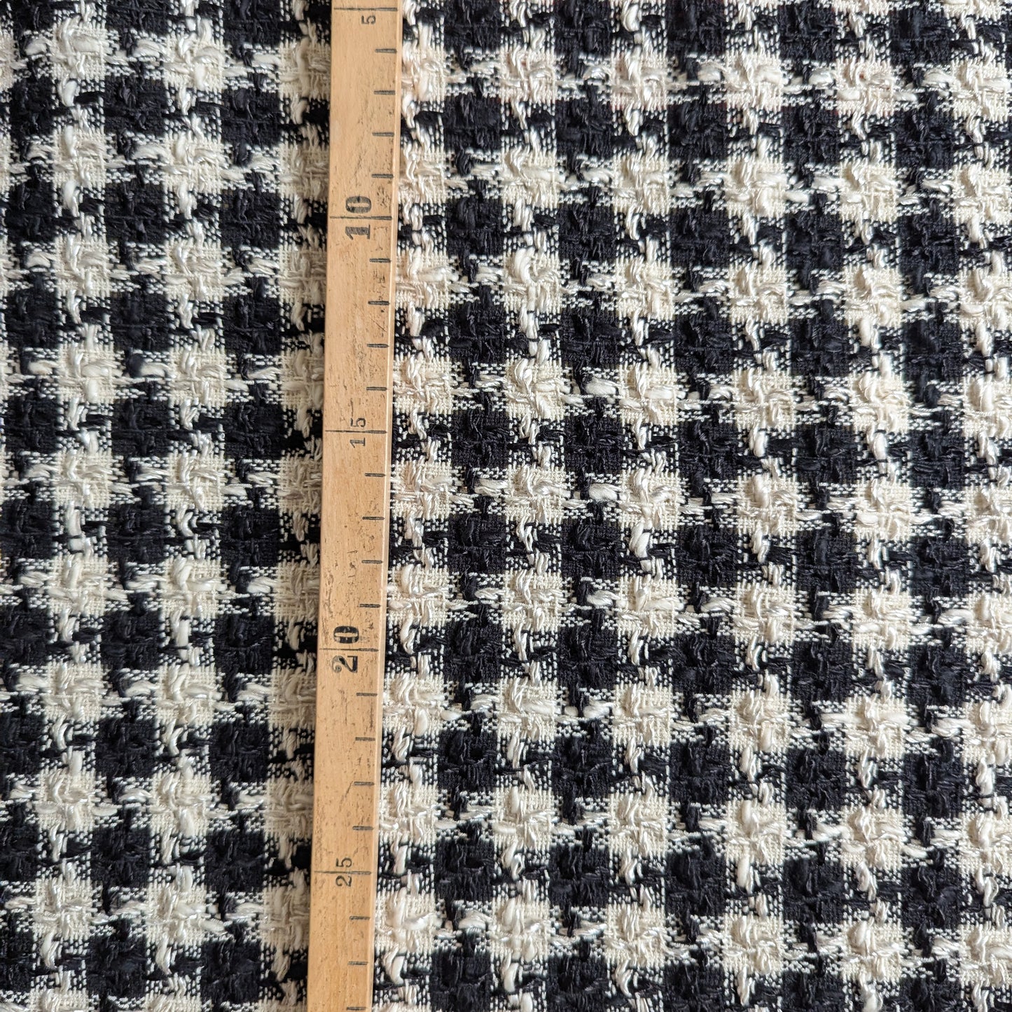 Black and white houndstooth wool tweed fabric with a wooden ruler showing measurements.