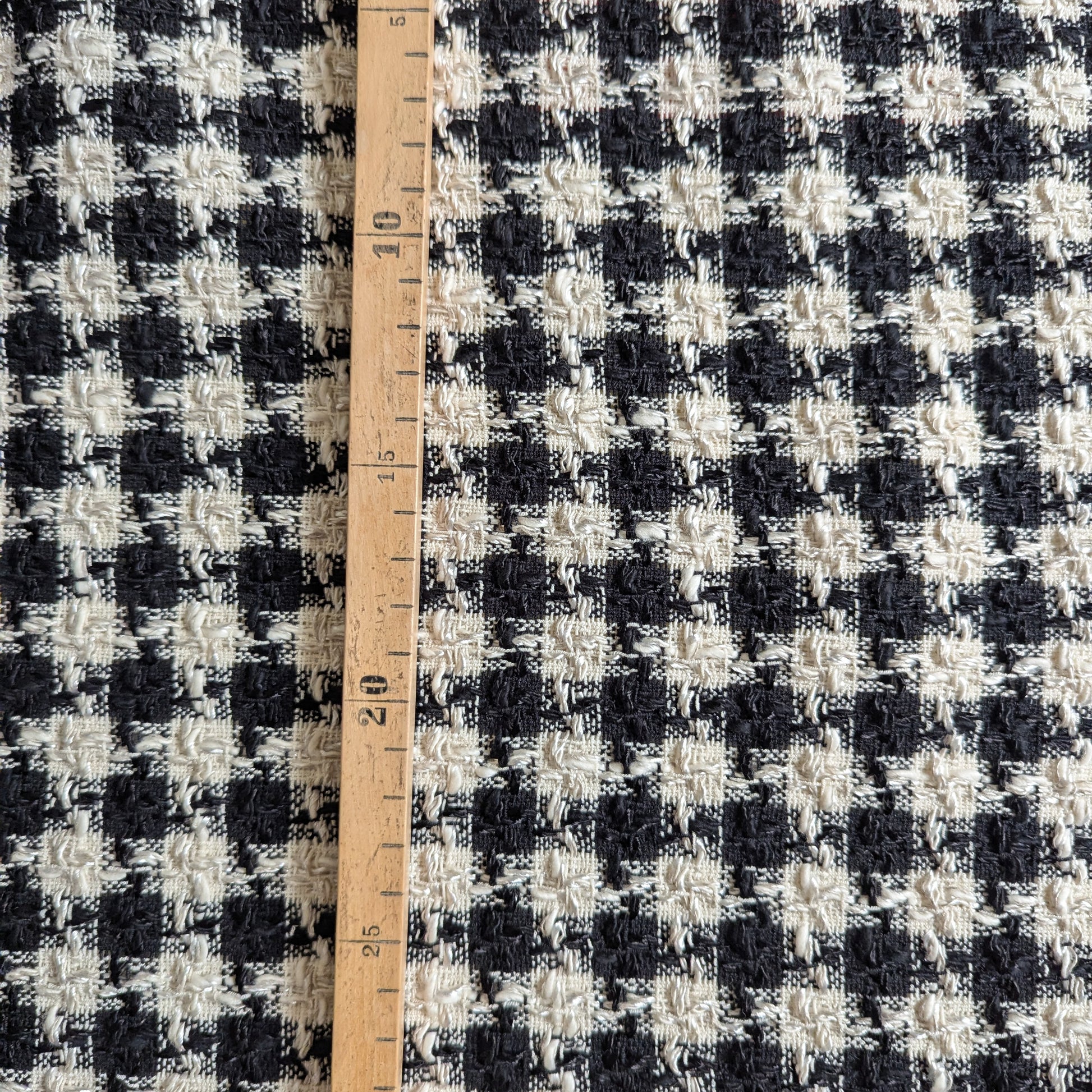 Black and white houndstooth wool tweed fabric with a wooden ruler showing measurements.