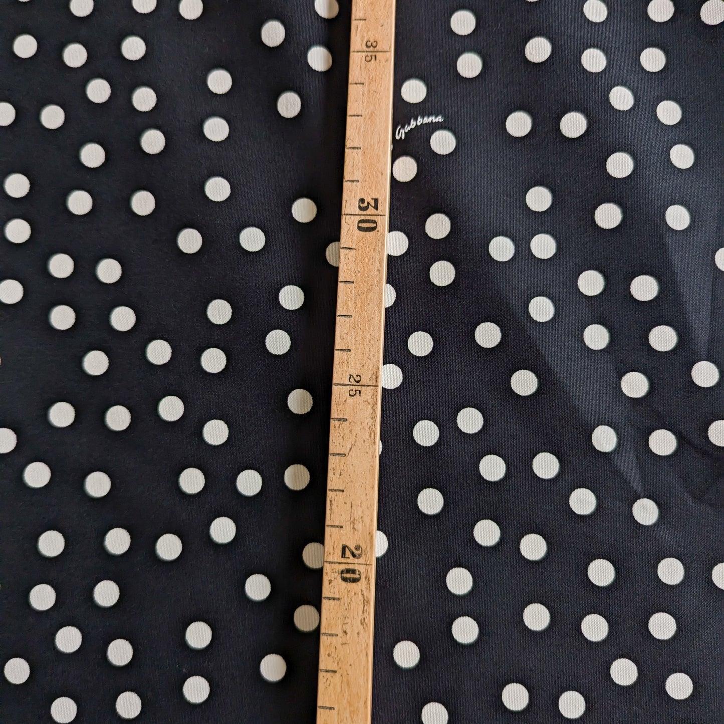 Black D&G deadstock cotton fabric with white polka dots, measured by a wooden ruler.