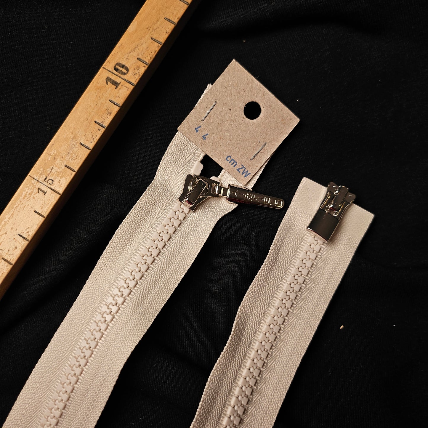 White 44 cm Airfield separable zipper with silver pull, next to a wooden ruler.