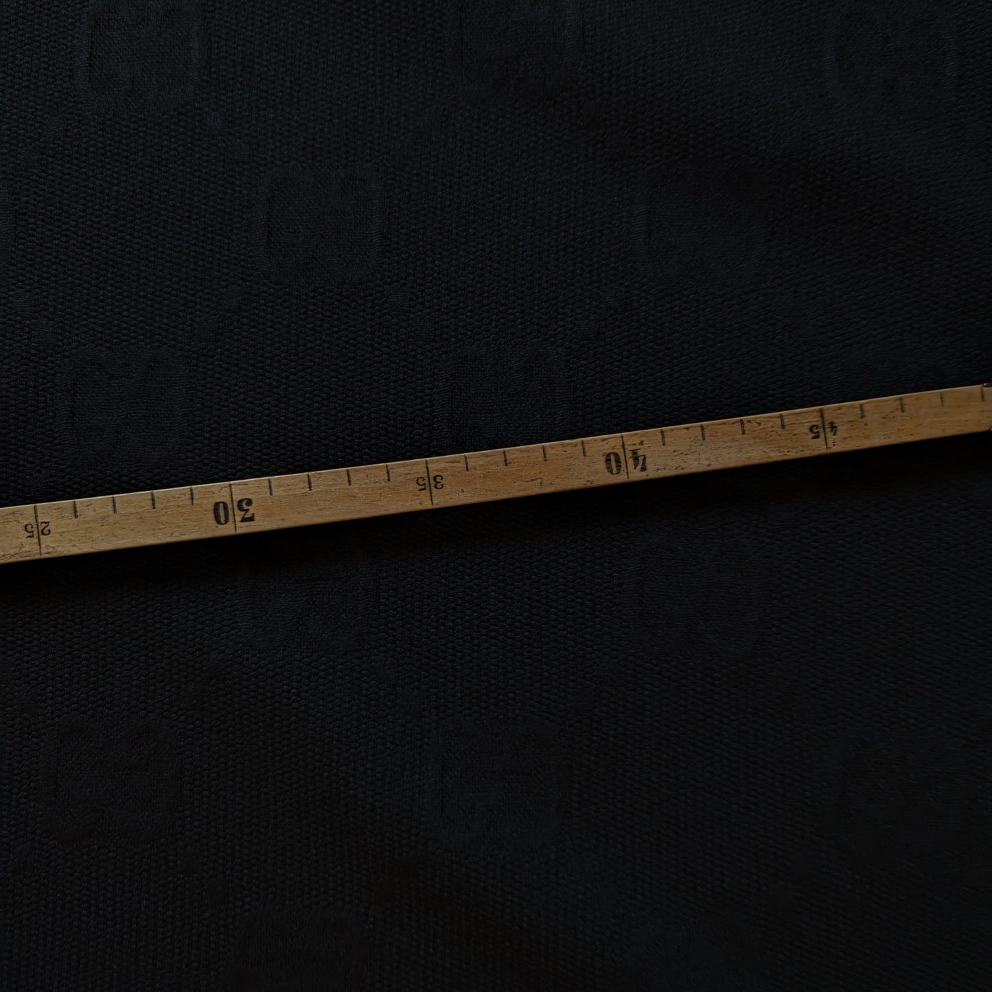 Black G*cci polyester jacquard fabric, textured with a woven tone-on-tone logo, measured by a wooden tape.
