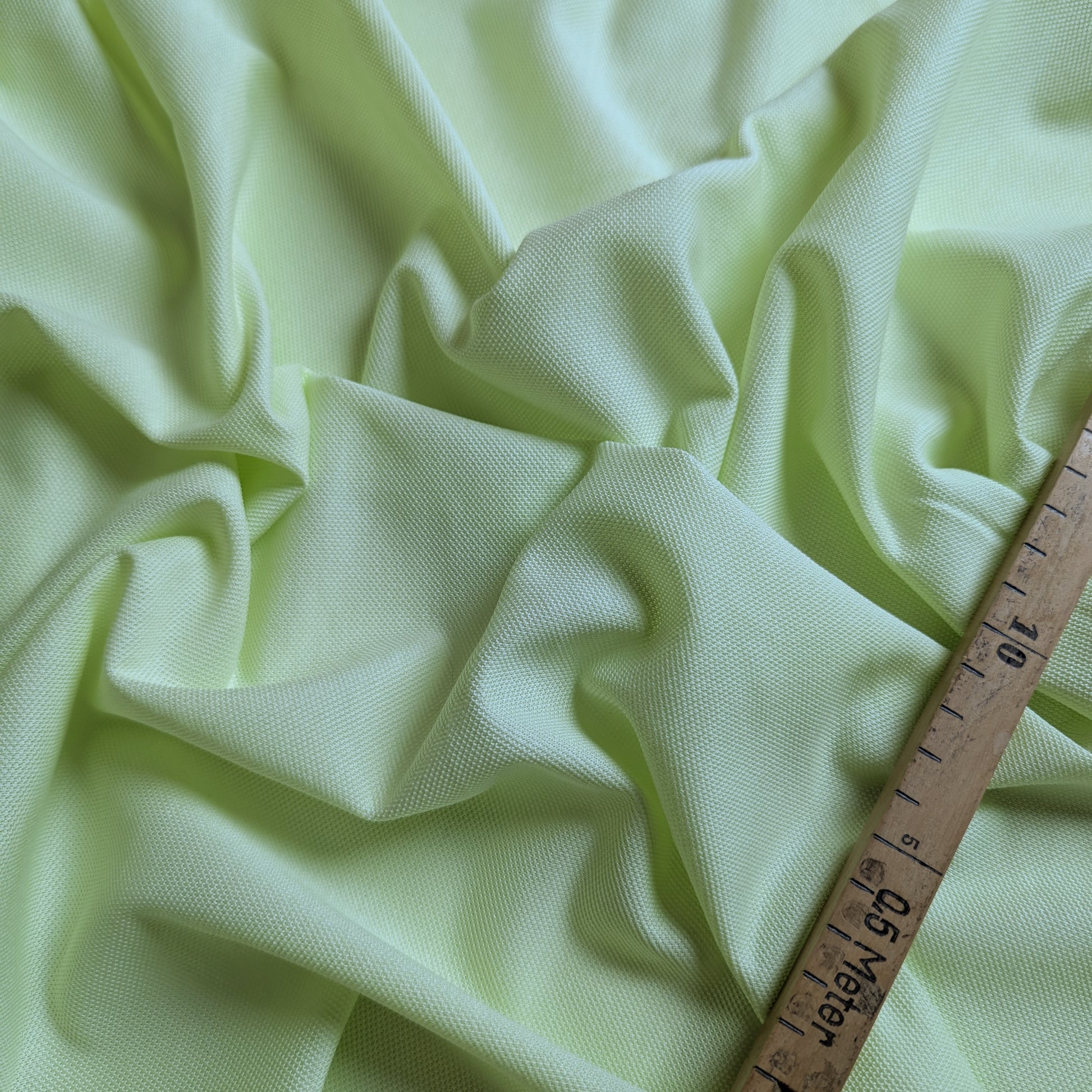 Draped lime green H*rm*s deadstock cotton piqué designer fabric with structured texture, measured by a ruler.