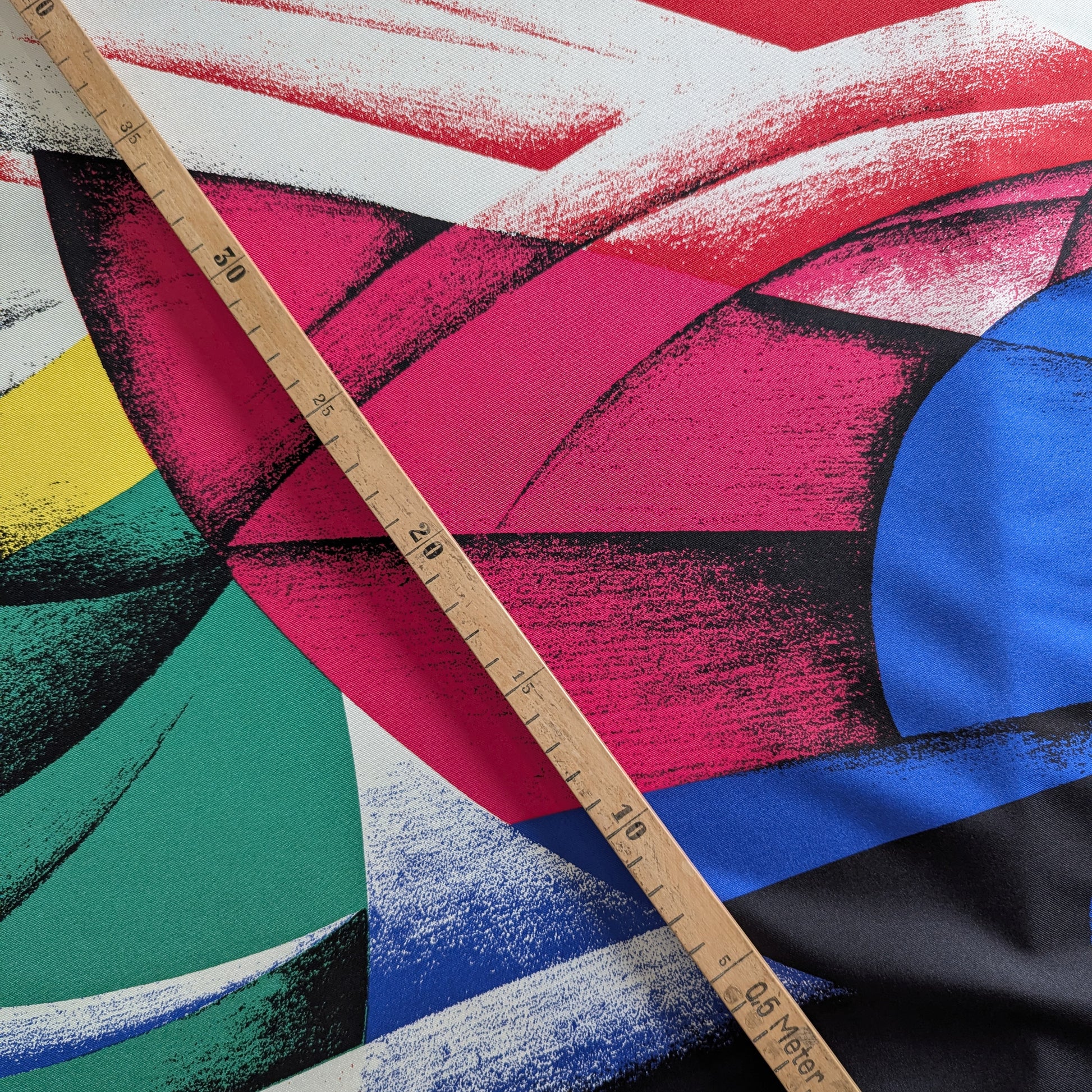 Versace deadstock silk fabric with a vibrant, multicolor XXL abstract print and a wooden ruler.