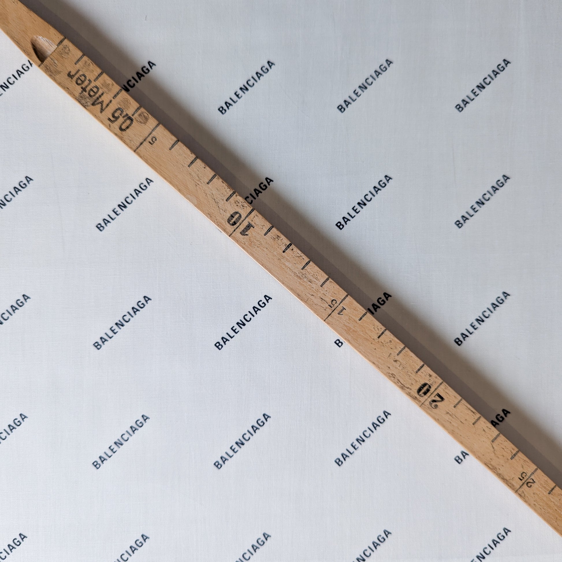 White Balenciaga cotton poplin deadstock fabric with logo print, measured by a wooden ruler.