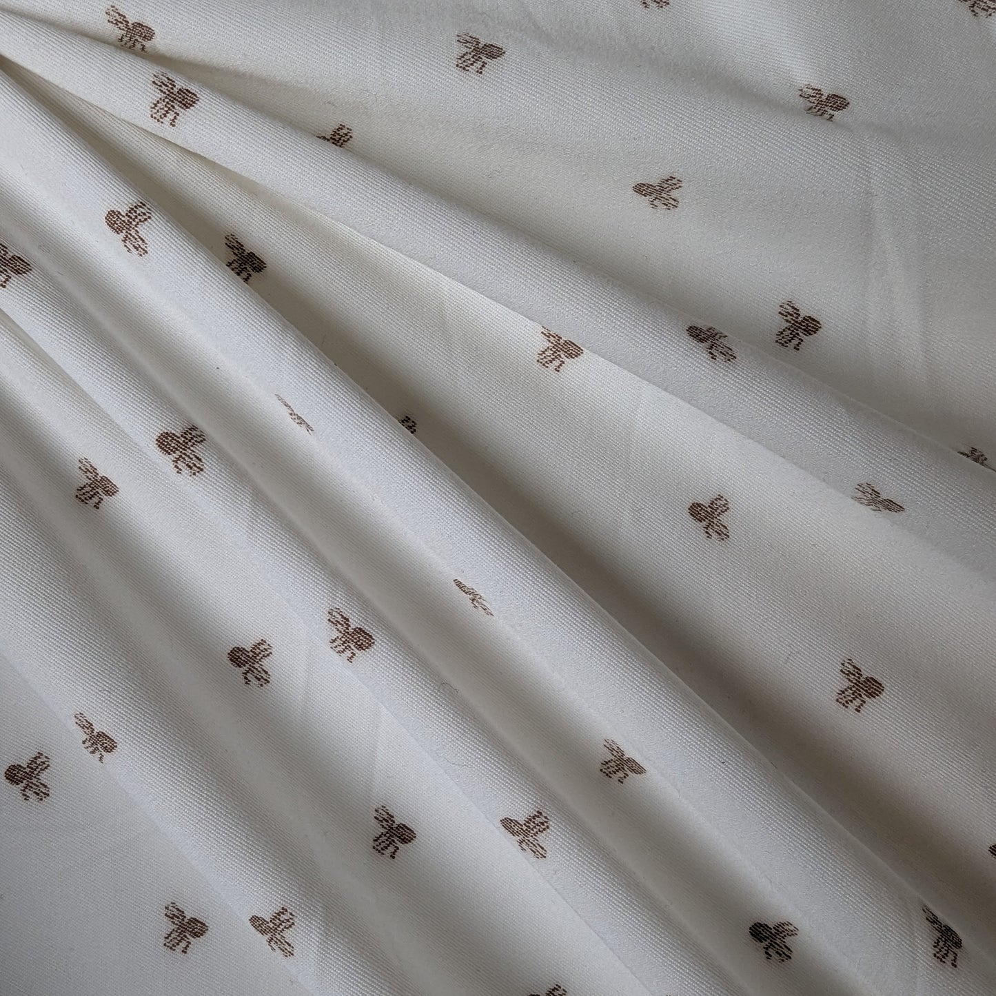 White deadstock cotton fabric with subtle brown fil coupé octopus motifs, draped.