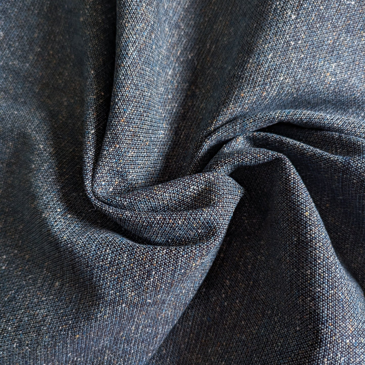 Dark blue cotton denim fabric with a coarse weave and subtle flecks, folded in a swirl.