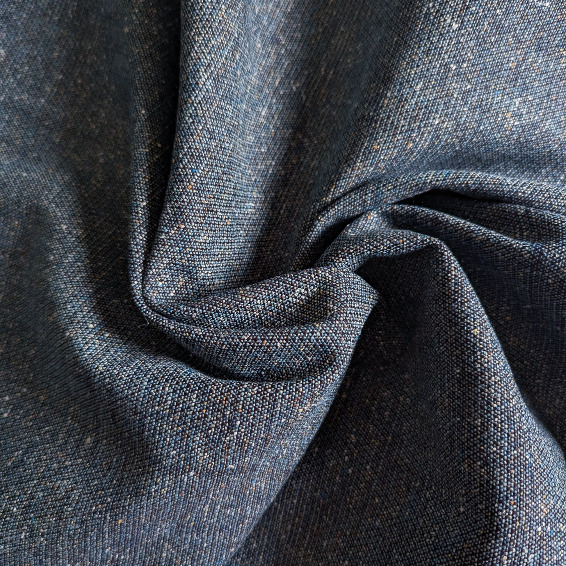 Dark blue cotton denim fabric with a coarse weave and subtle flecks, folded in a swirl.