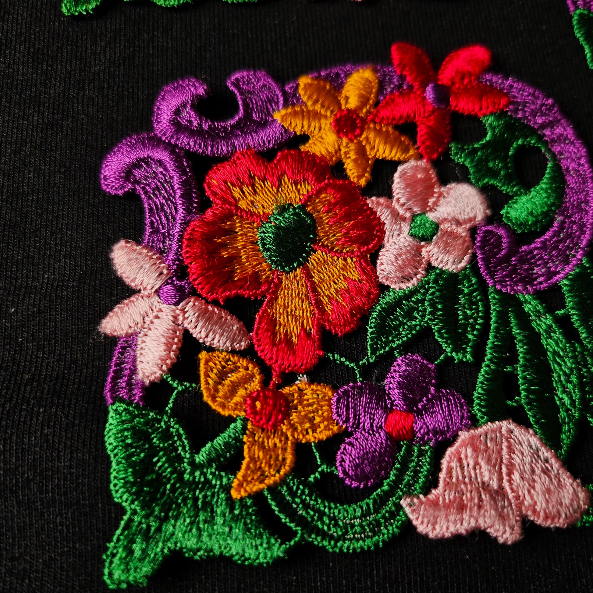Colorful embroidered floral patch with red, yellow, pink, purple, and green threads on black fabric.