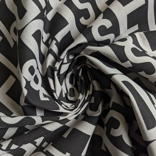 Dark grey designer cotton-denim with a bold light grey abstract letter pattern, folded and swirled.