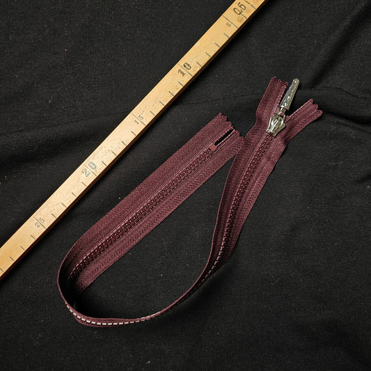 Airfield 42 cm non-separable wine red zipper with silver pull on black fabric, next to a wooden ruler.