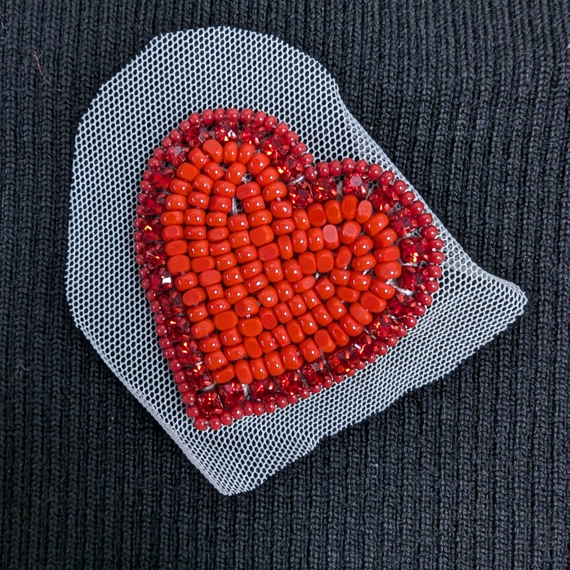 Red crystal heart patch on white mesh, featuring hand-sewn, sparkling stones on a dark fabric.