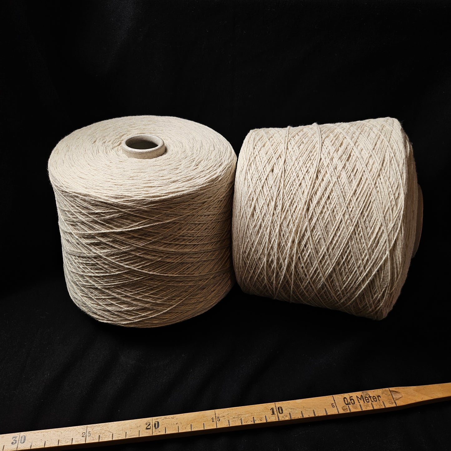 Two large cones of natural white 50% yak, 50% merino yarn on a black background with a ruler.