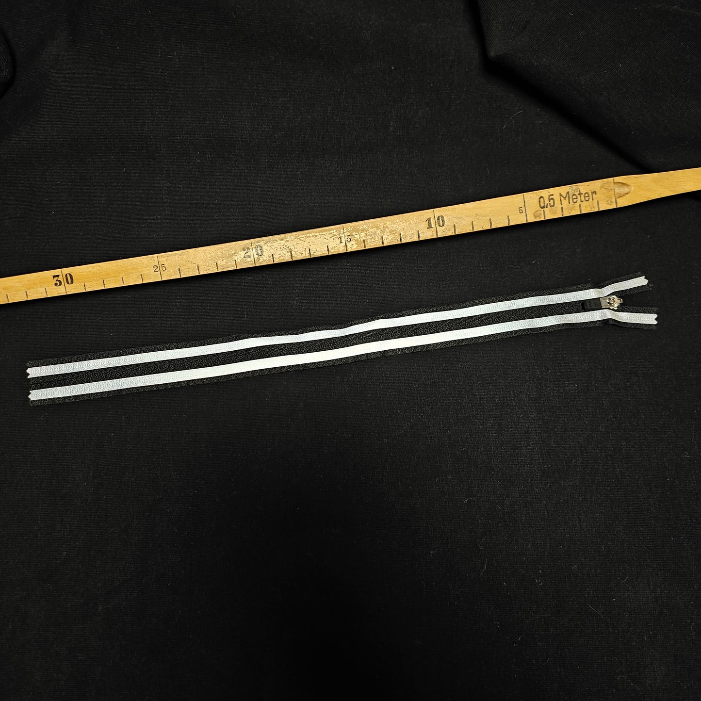 Black designer zipper, 30 cm, with white stripes on a black fabric background.