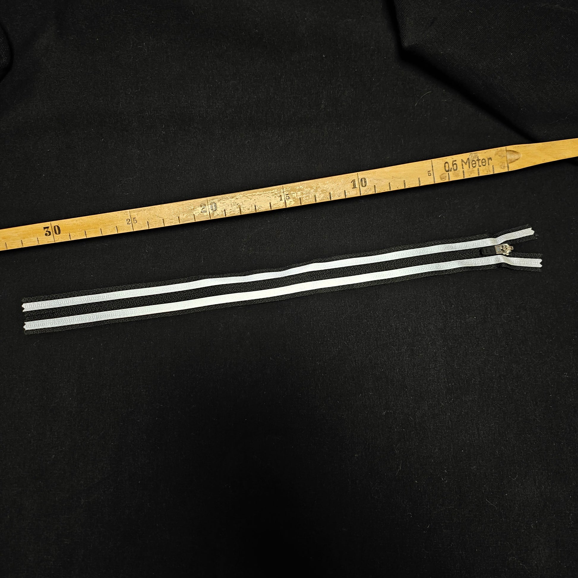Black designer zipper, 30 cm, with white stripes on a black fabric background.