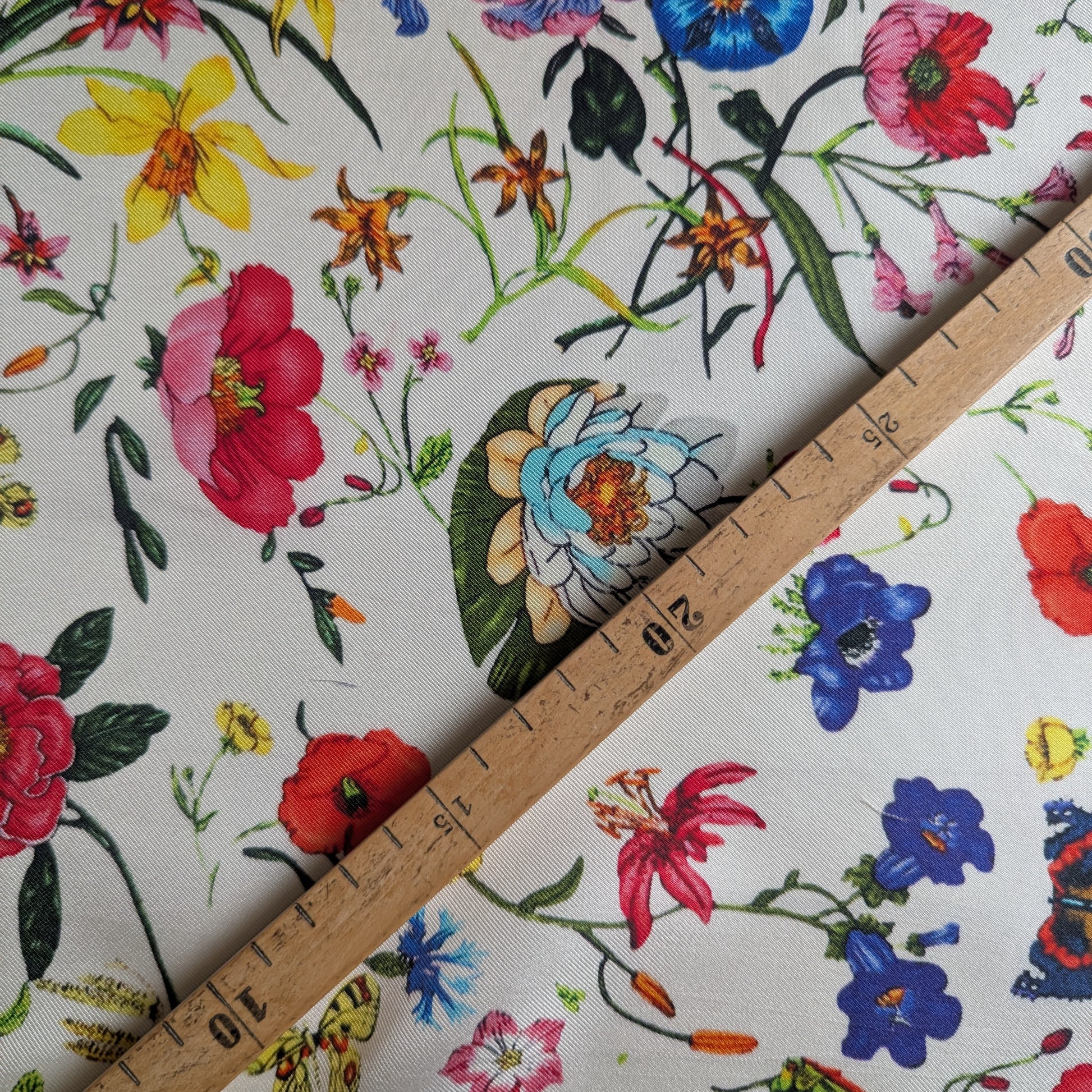 White deadstock silk twill fabric with a vibrant floral garden print and a wooden ruler.