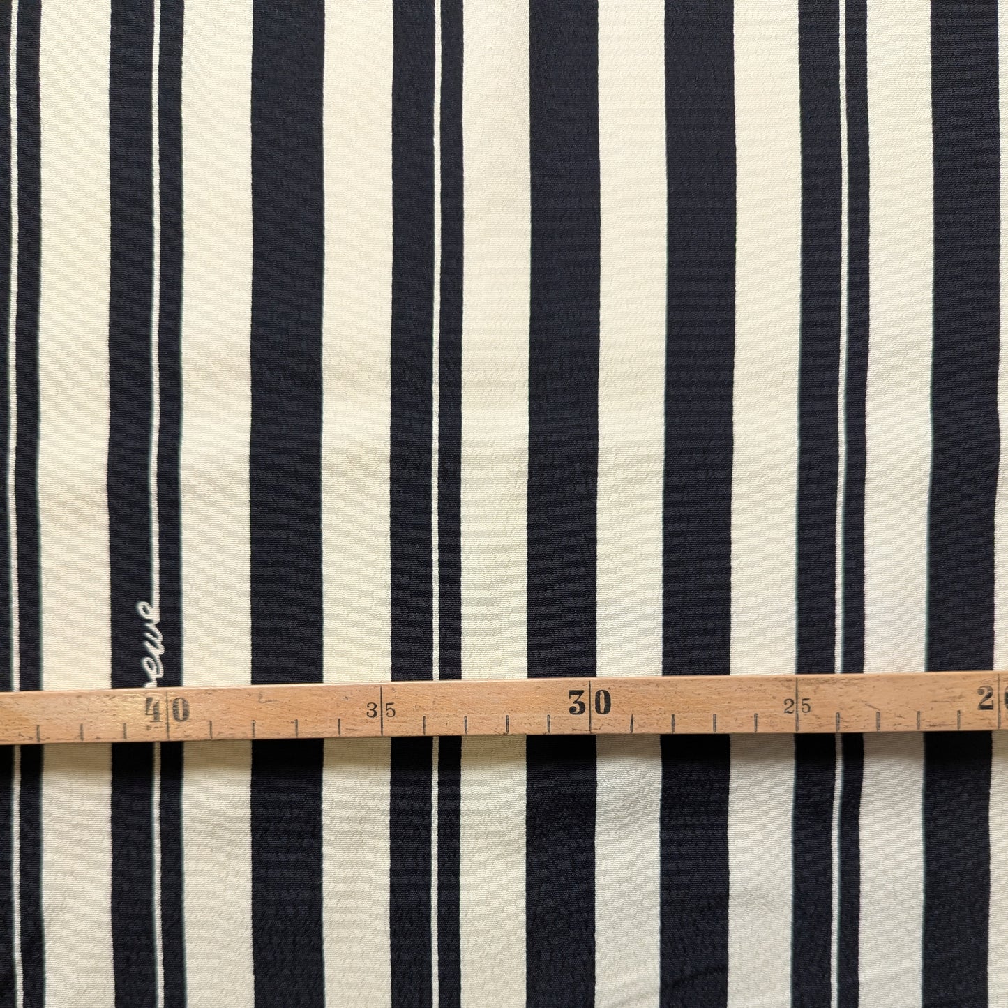 Viscose crepe fabric with natural white and black vertical stripes, measured by a wooden ruler.