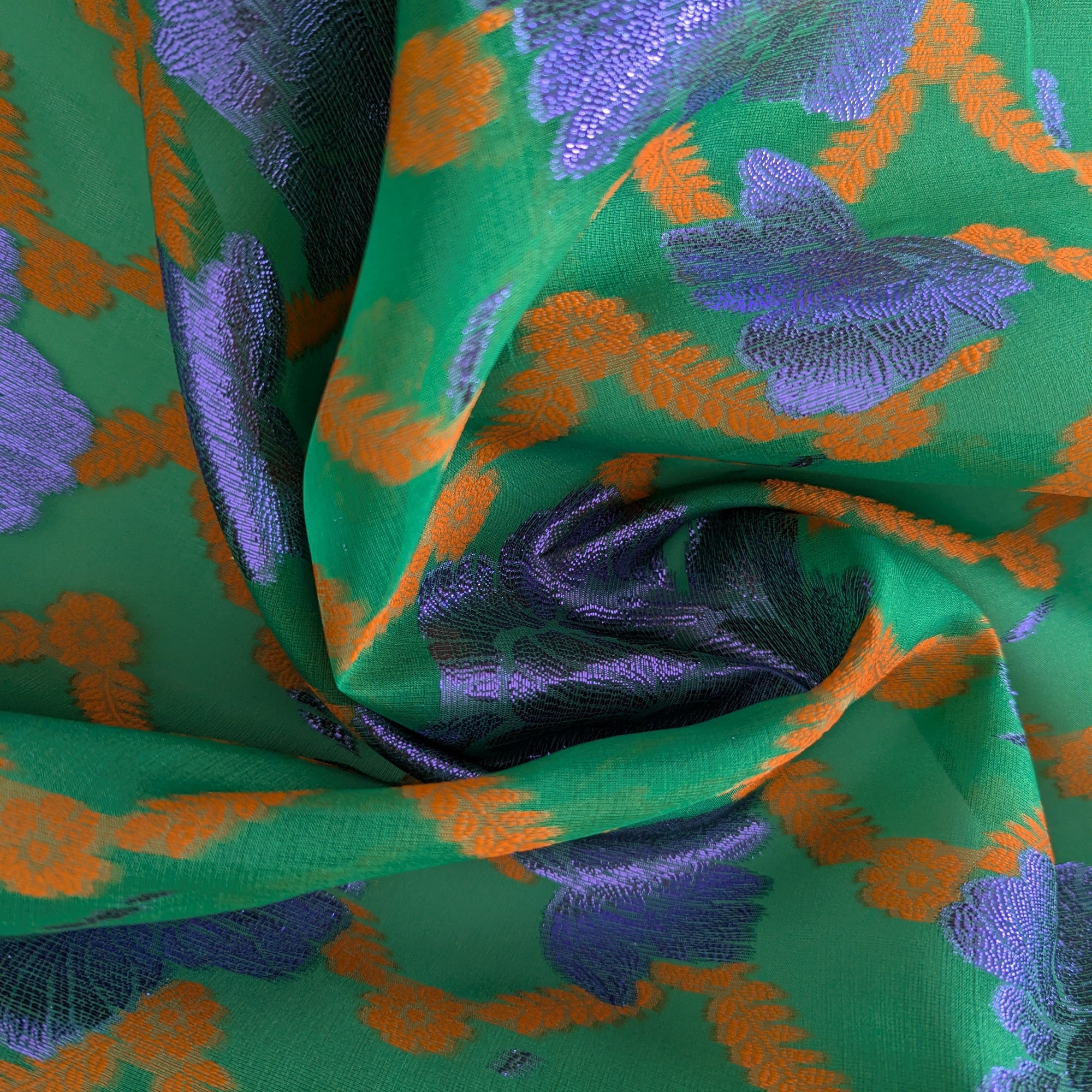 Vibrant green jacquard silk fabric with shimmering purple and orange Lurex floral pattern, elegantly draped.