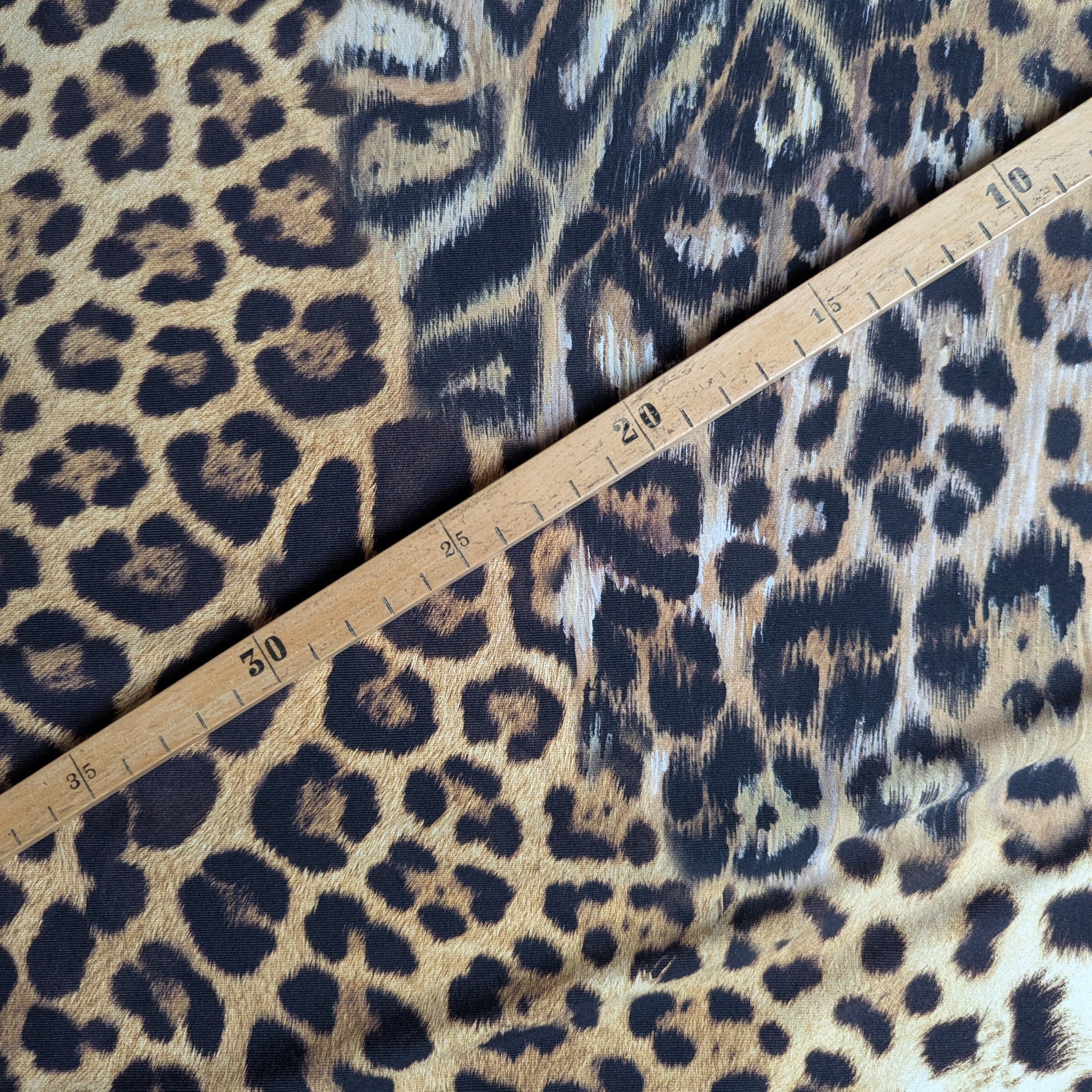 Elastic brown and black leopard print Lycra fabric with a wooden ruler showing measurements.