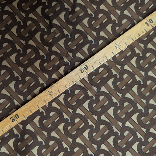 Brown B*rberry logo cotton poplin fabric with a wooden ruler across it.