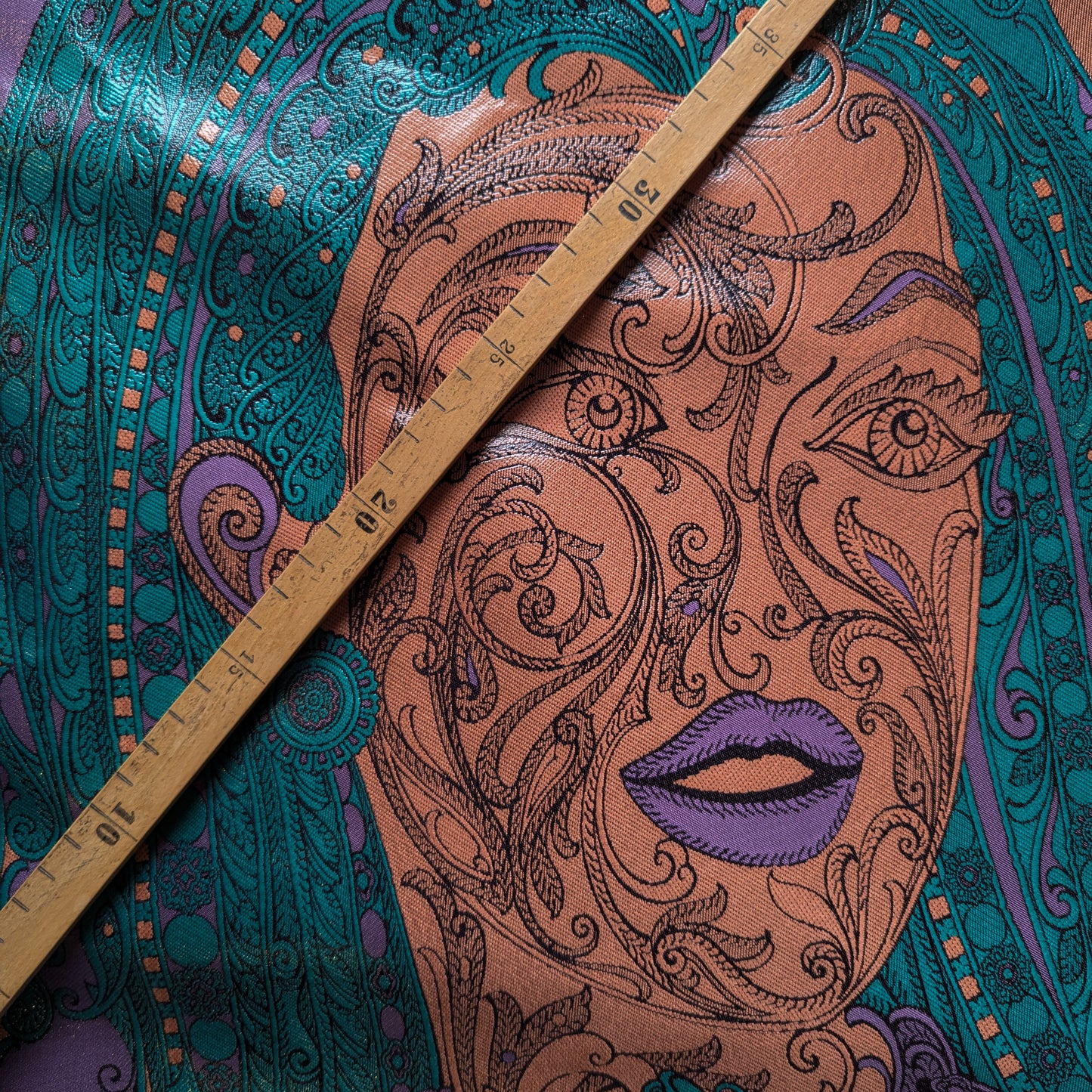 Multicolor polyester deadstock fabric with a detailed face design in purple, pink, and green, measured by a ruler.