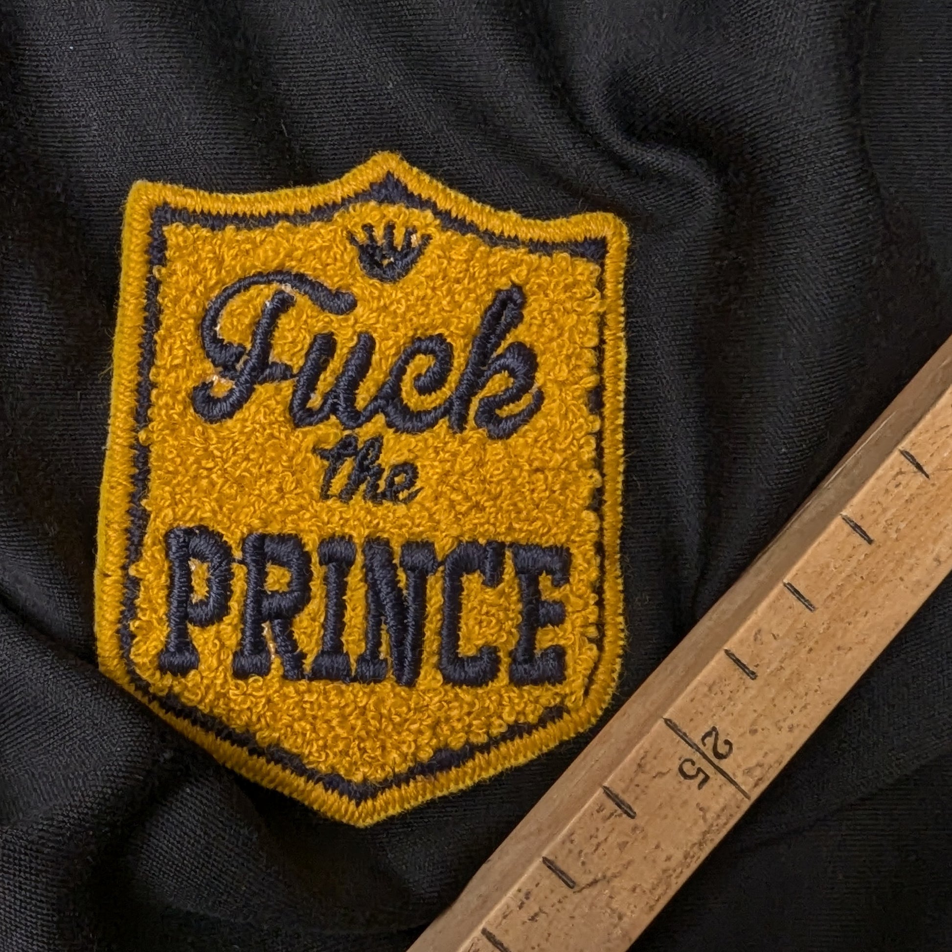 Mustard yellow D&G "Fuck the Prince" patch with 3D terrycloth texture and dark blue embroidery.
