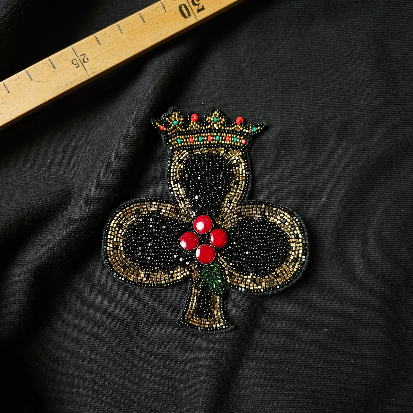 Black beaded clover patch with a gold and red crown, red berries, and green leaves.
