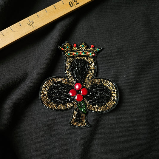 Black beaded clover patch with a gold and red crown, red berries, and green leaves.