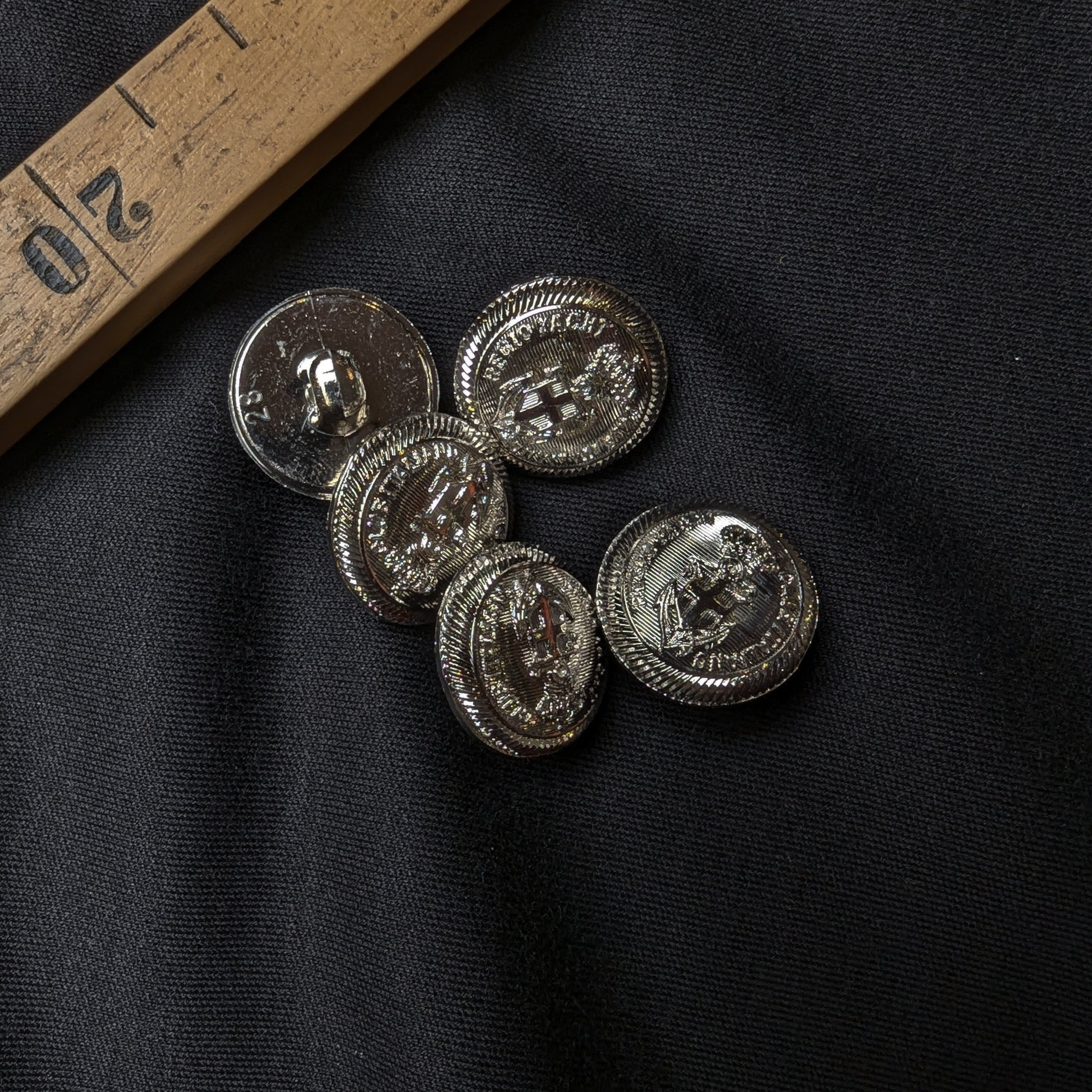 Five shiny silver plastic buttons, 1.5 cm, with an embossed anchor design on black fabric.