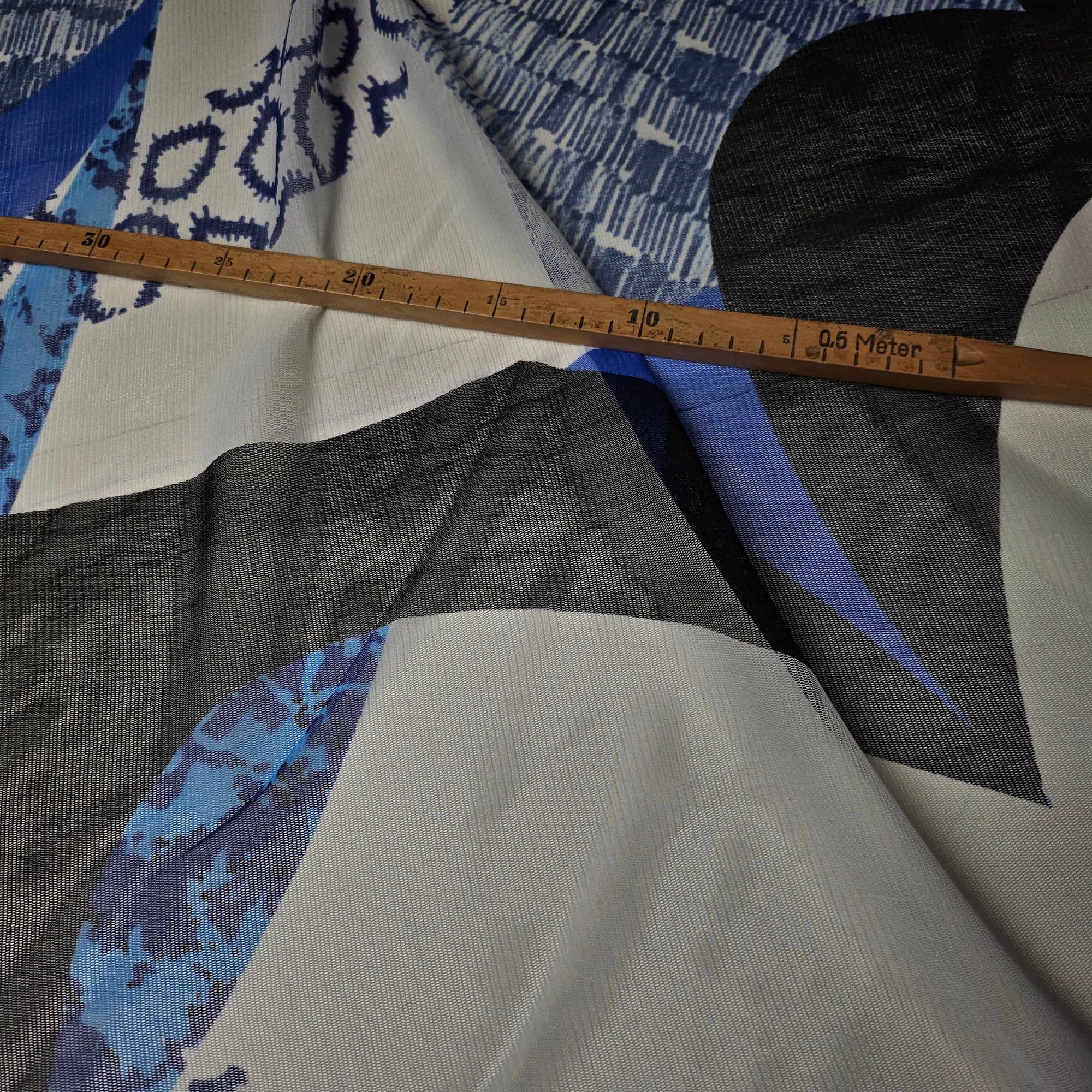 Bright white deadstock fine tulle fabric with abstract black and blue print, transparent and lightweight, ruler for scale.