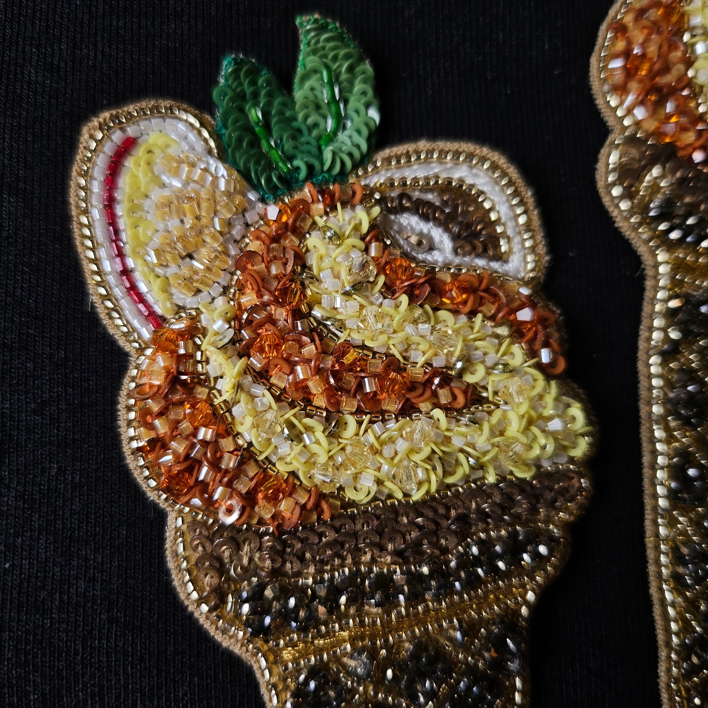Embroidered ice cream patch with colorful beads, sequins, and green leaves on a black background.