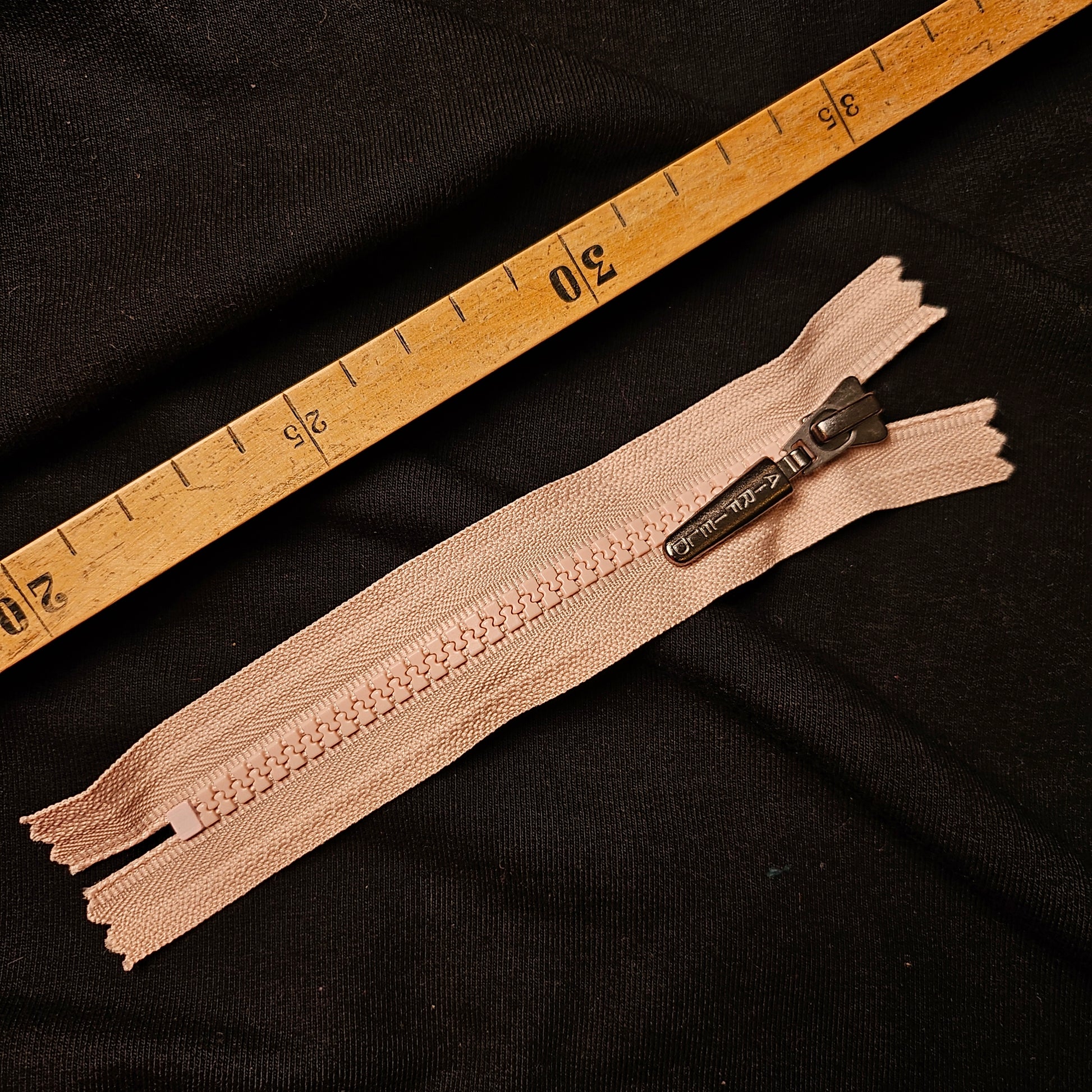 Airfield 17 cm non-separable light pink zipper with a metallic pull tab, shown on black fabric next to a wooden ruler.