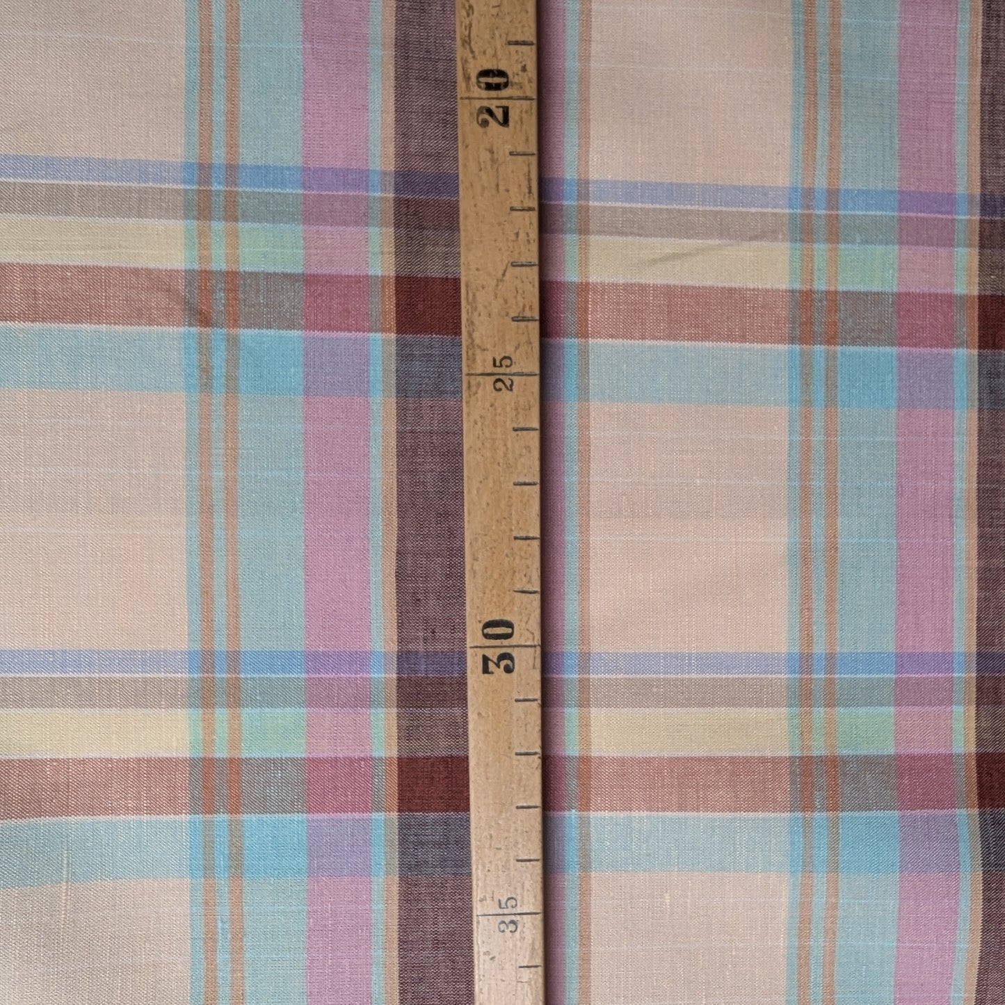 Gucci deadstock cotton-linen tartan fabric in beige, brown, blue, and pink plaid with a wooden ruler.