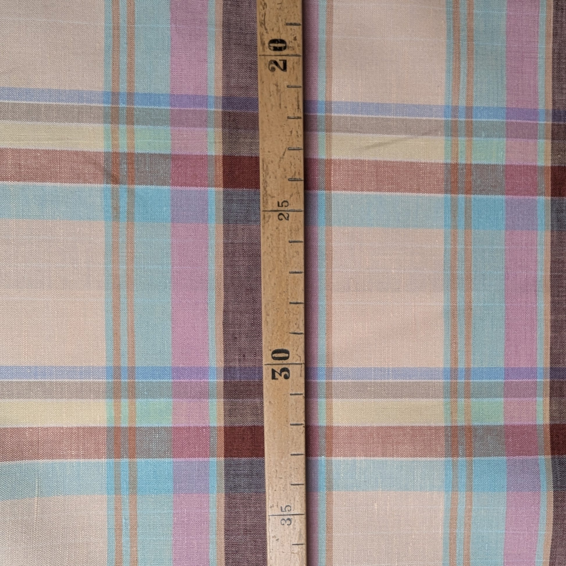 Gucci deadstock cotton-linen tartan fabric in beige, brown, blue, and pink plaid with a wooden ruler.