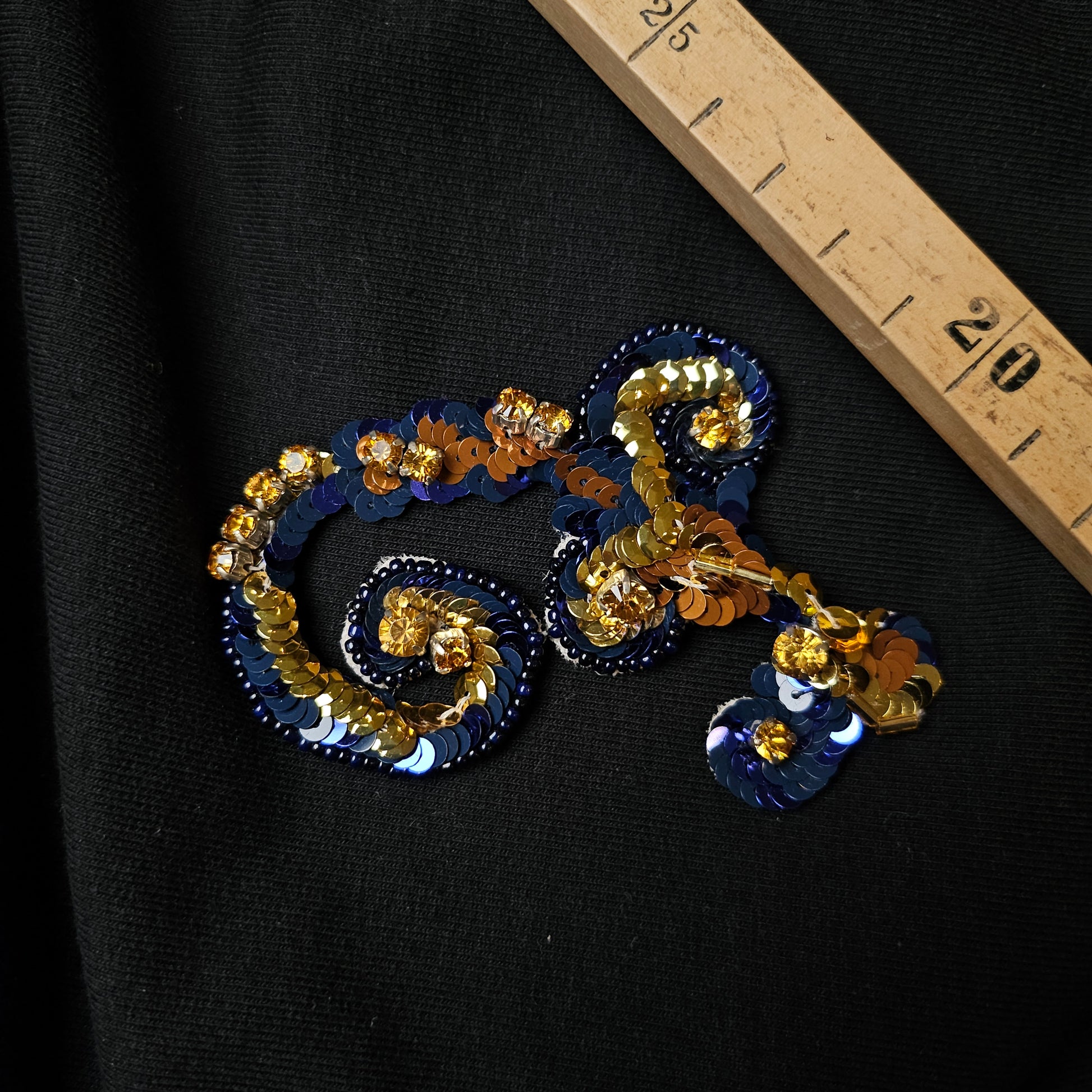 Blue and gold sequin D&G ornament patch, 9x5.5cm, on black fabric with a wooden ruler.
