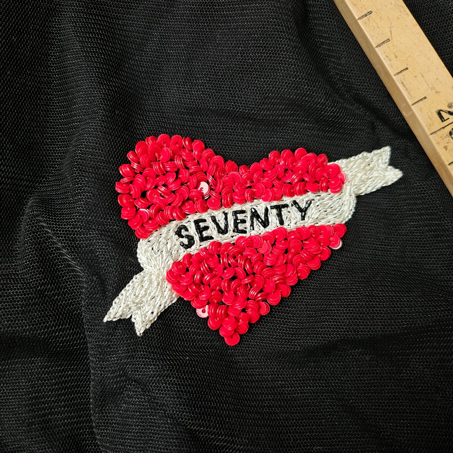 Red sequin heart patch with "SEVENTY" on a white banner, on black fabric.