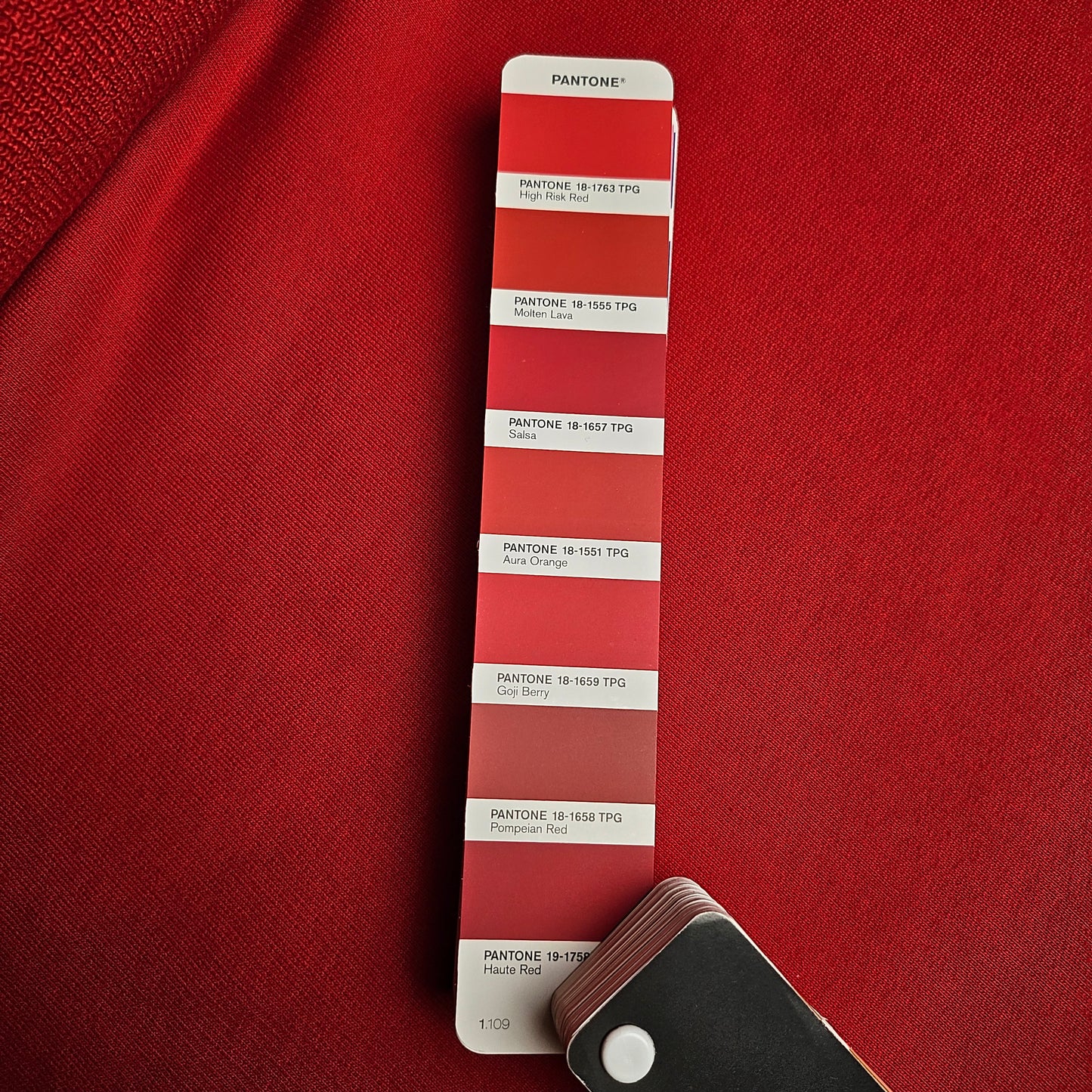 Vibrant tomato red deadstock cotton sweatshirt fabric with a subtle sheen, next to a Pantone color swatch.