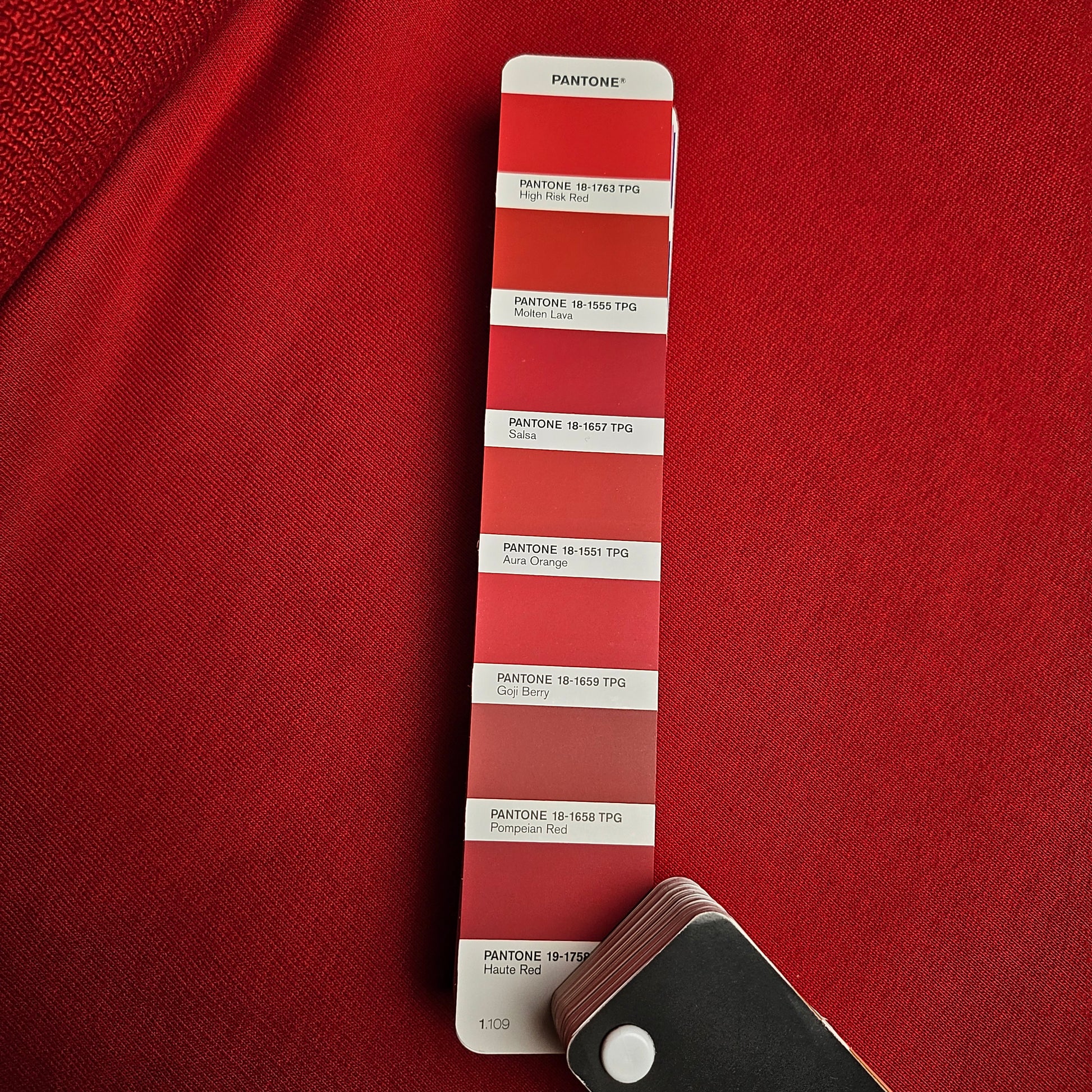 Vibrant tomato red deadstock cotton sweatshirt fabric with a subtle sheen, next to a Pantone color swatch.