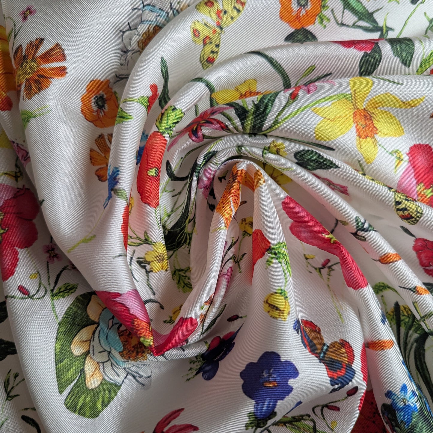 White deadstock silk twill fabric with a vibrant floral and butterfly garden print, elegantly draped.