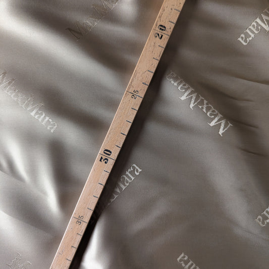 Beige Max Mara deadstock viscose lining fabric with subtle logo print, measured by a wooden ruler.