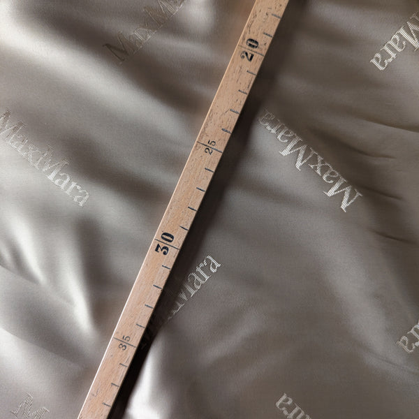 Beige Max Mara deadstock viscose lining fabric with subtle logo print, measured by a wooden ruler.