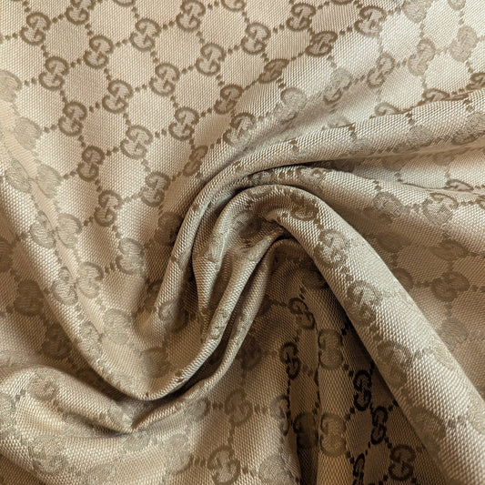 High-quality camel G*cci deadstock cotton-polyester jacquard fabric with woven GG logo, draped.