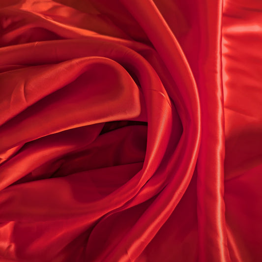 Vibrant red viscose lining fabric, softly draped and folded, showing its smooth texture.