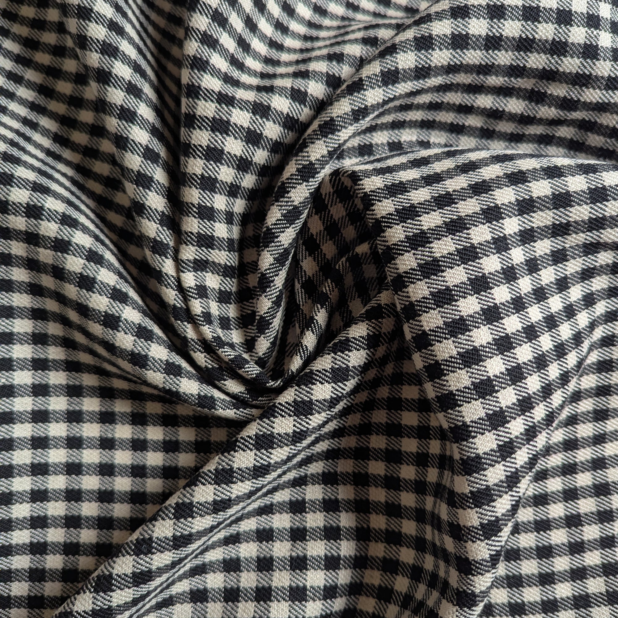 Swirled deadstock wool fabric with a black and off-white gingham check pattern, showing textured weave.