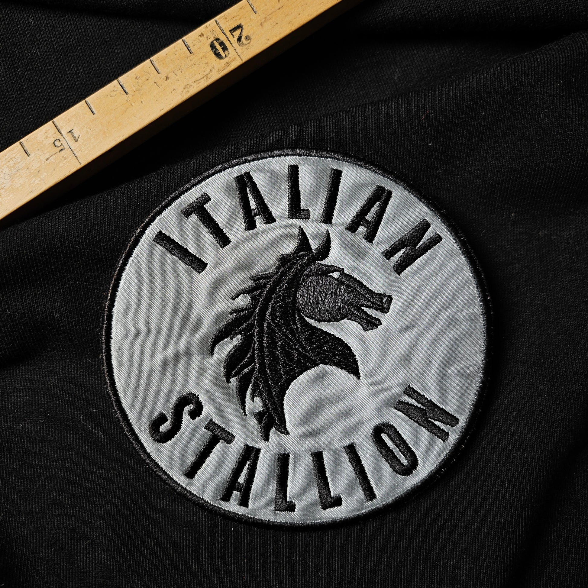 Round D&G "Italian Stallion" patch with black horse embroidery on light gray, 10x10 cm, on black fabric.